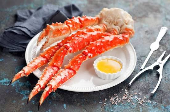 Cooked king crab legs on a white plate with butter, seafood cracker, and pick on a dark slate background